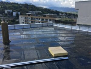 Toiture plate recouverte d’une membrane bitumineuse noire avec outils de chantier posés, illustrant des travaux d’étanchéité en cours.